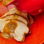 Gravy pouring on to slices of turkey on a red plate