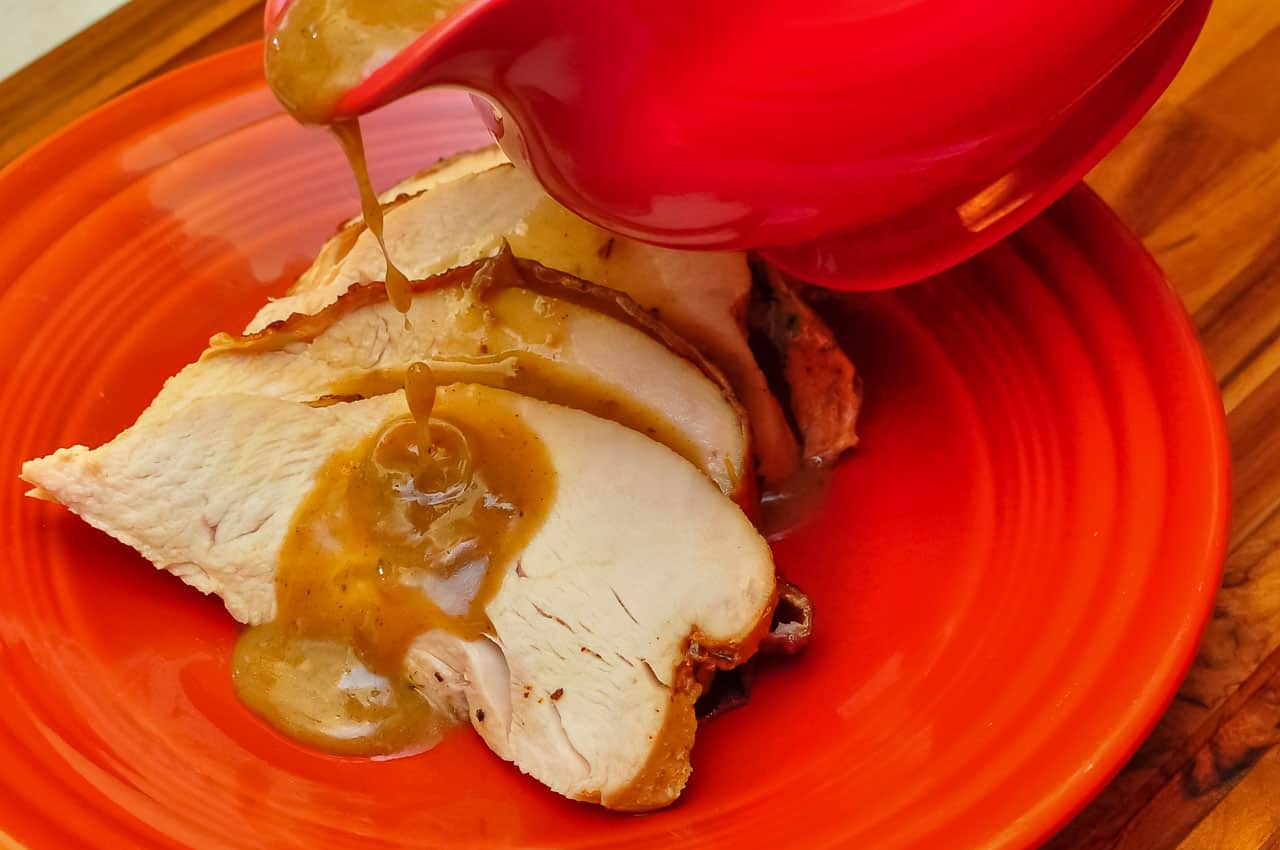 Gravy pouring on to slices of turkey on a red plate