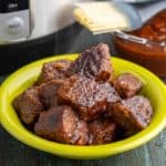 A bowl full of cooked brisket cubes, glazed with barbecue sauce, with an Instant Pot and a bowl of barbecue sauce in the background