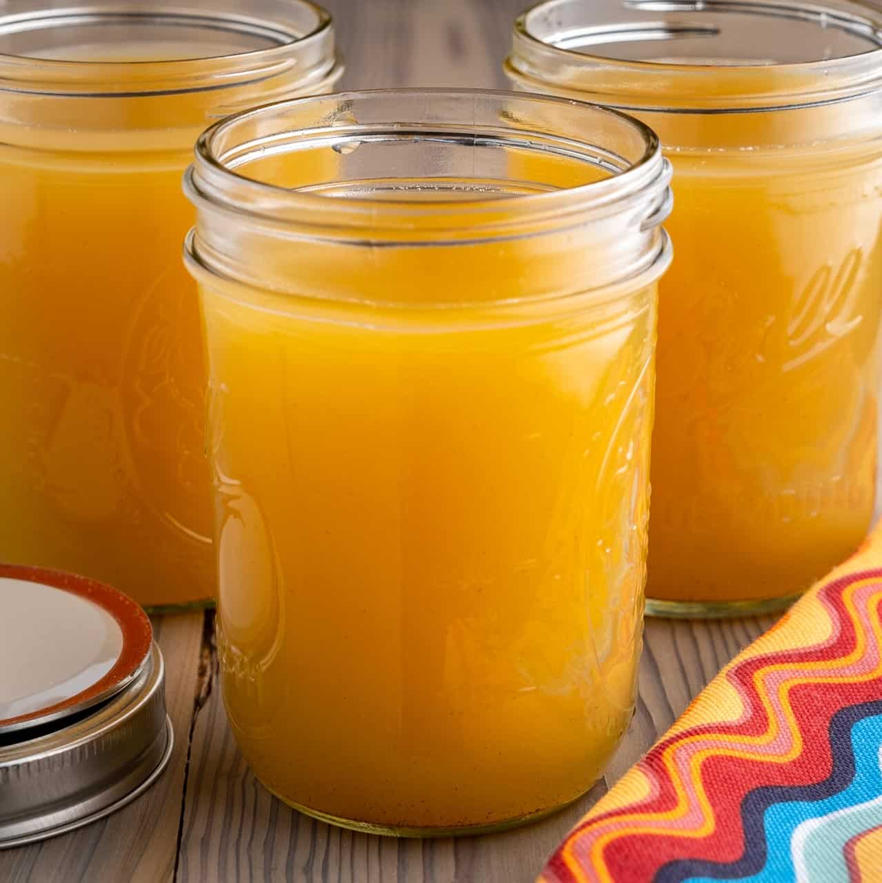 Canning jars full of bone broth with a napkin and a canning jar lid in the foreground