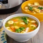 A bowl of turkey tortellini soup with carrots, spinach, tomatoes, and celery, with an instant pot visible in the background