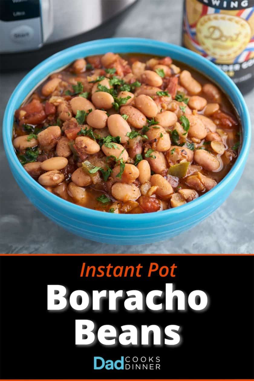 A blue bowl of borracho beans, pinto beans with bacon, tomato, and jalapeno, sprinkled with minced cilantro, with a bottle of beer and an Instant Pot in the background.