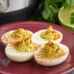 Four guacamole deviled eggs on a maroon plate, with an Instant Pot and cilantro and a lime in the background