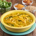 A yellow bowl of rotisserie chicken and lentil soup, with spices and herbs in the background