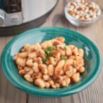 A bowl of cooked yellow eye beans on a wood table with an Instant Pot and some uncooked beans in the background