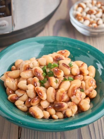 A bowl of cooked yellow eye beans on a wood table with an Instant Pot and some uncooked beans in the background