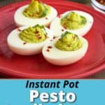 Four pesto deviled eggs, with green filling, sprinkled with basil and red pepper flakes, on a maroon plate