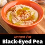 A bowl of black-eyed pea hummus, drizzled with olive oil and sprinkled with paprika, with a bowl of paprika, black-eyed peas, and garlic in the background