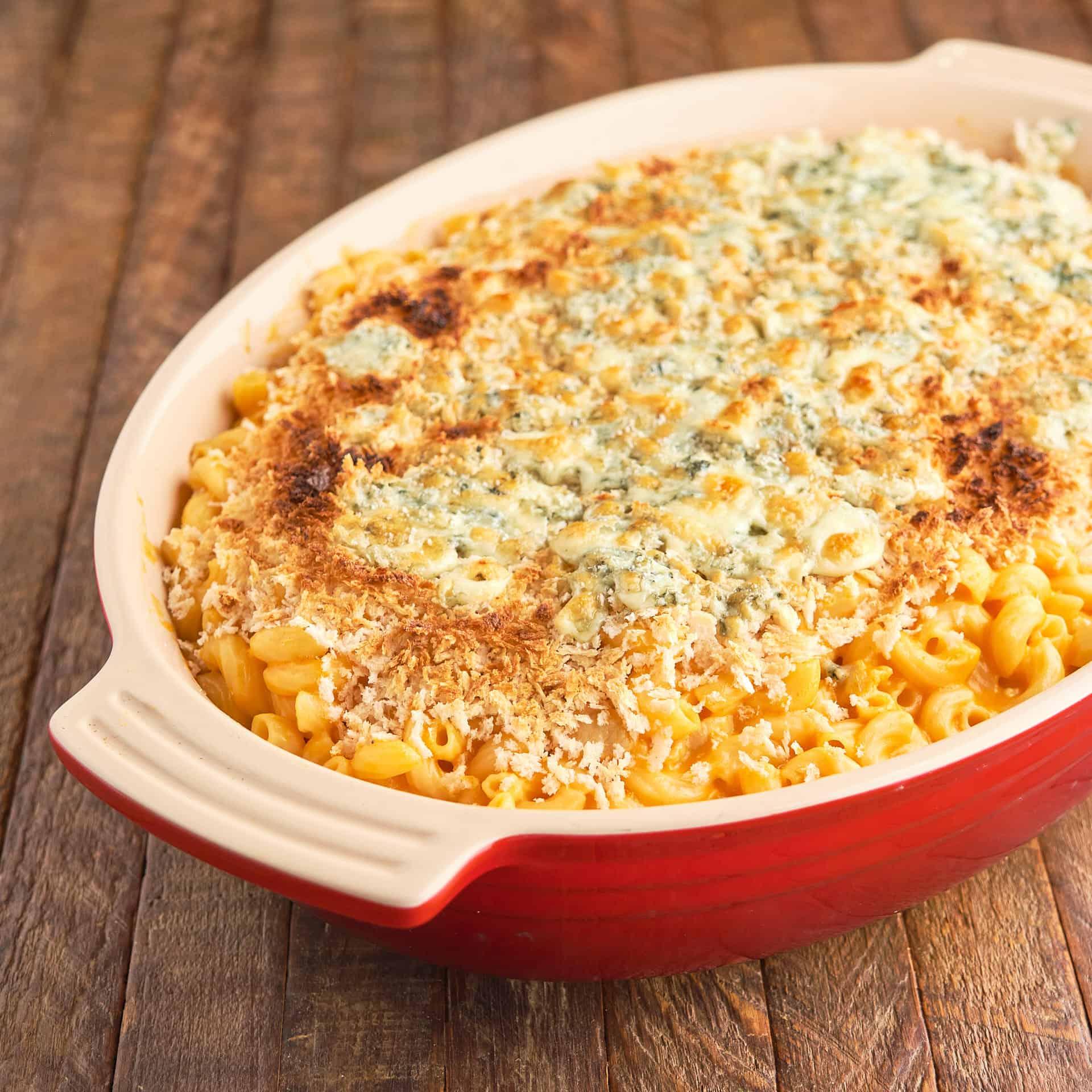 A red baking dish full of Instant Pot Buffalo Chicken Mac and Cheese, topped with a browned crust of breadcrumbs and blue cheese