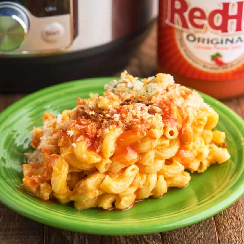 A plate of buffalo chicken mac and cheese in front of an Instant Pot and a bottle of Franks RedHot