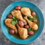 A bowl of cooked chicken drumsticks and baby red potatoes, with parsley leaves
