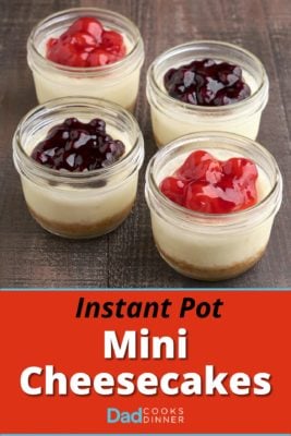 Four mini cheesecakes in canning jars, with cherry and blueberry topping, on a wood tabletop