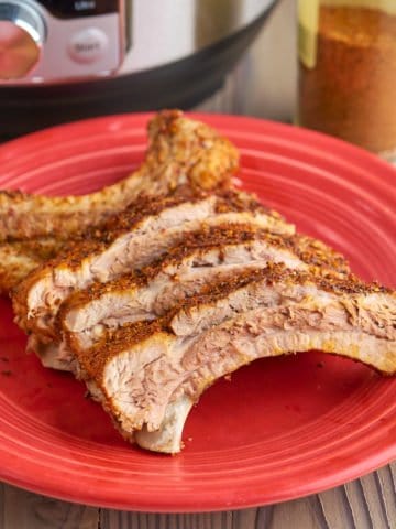 Baby back ribs with dry rub on a red plate, with an Instant Pot and a jar of dry rub in the background