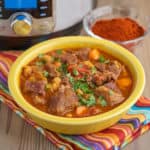 A bowl of Spanish beef stew in front of a dish of smoked spanish paprika - pimenton de la Vera - and an Instant Pot