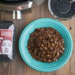 A bowl of cooked beluga lentils, next to a bowl and bag of uncooked lentils, and an Instant Pot