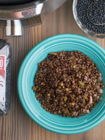 A bowl of cooked beluga lentils, next to a bowl and bag of uncooked lentils, and an Instant Pot