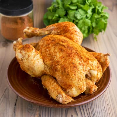 A whole chicken sprinkled with Cajun Spice Rub, on a plate, with more spice rub and some parsley in the background