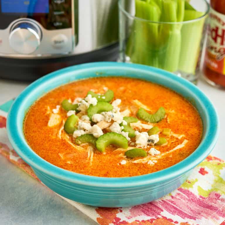 A bowl of Buffalo chicken soup topped with celery and blue cheese crumbles, with an Instant Pot and celery sticks in the background.