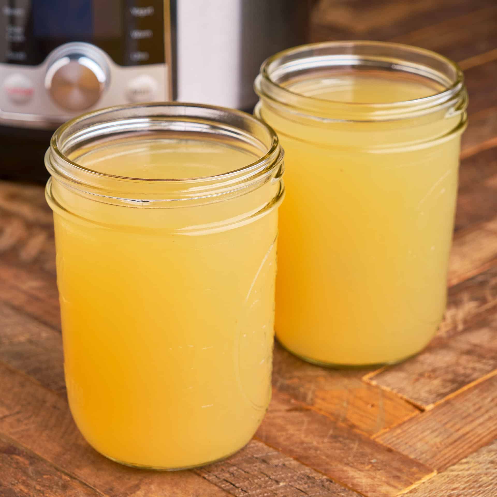 Two jars of chicken broth on a wood table in front of an Instant Pot