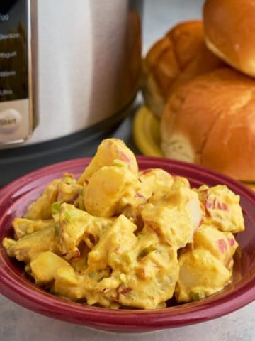 A bowl of mustard potato salad in front of a plate of hamburger buns and an Instant Pot