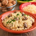 A bowl of mushroom risotto, with mushrooms, cheese, and parsley in the background