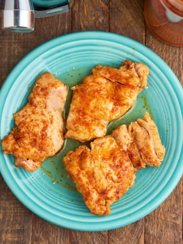 A plate of cooked chicken thighs, with an Instant Pot and a jar of paprika
