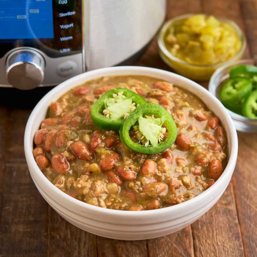 A bowl of green pork chili, with sliced jalapenos, and an Instant Pot in the background