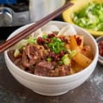 A bowl of Chinese beef noodle soup, with green onions and chili crisp