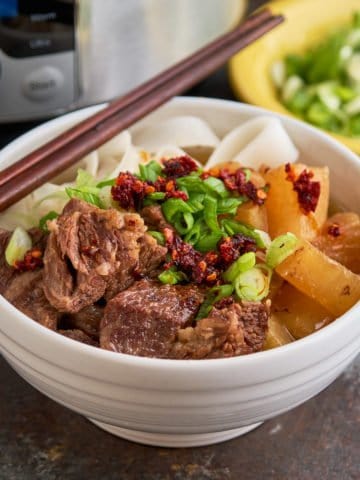 A bowl of Chinese beef noodle soup, with green onions and chili crisp