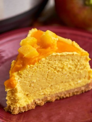 A slice of mango cheesecake on a maroon plate