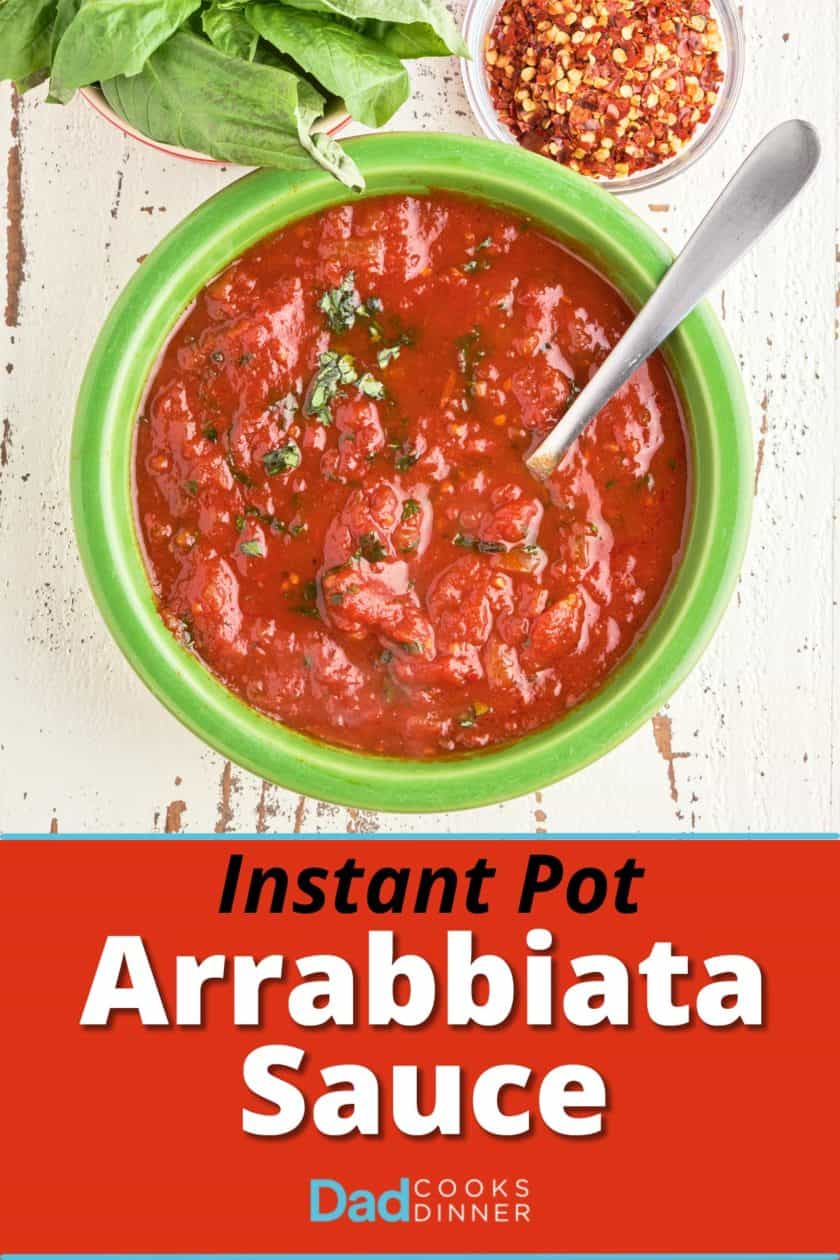 A bowl of arrabbiata sauce sprinkled with slivered basil, and a spoon sticking out of it, with a bowl of pepper flakes and a bowl of basil.