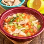 A bowl of lemon turkey and orzo soup, with a sprig of thyme, and a lemon and shredded turkey in the background