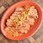 A platter of sliced brisket, covered with onions and tomatoes, on a wood table