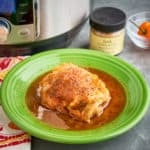 A chicken thigh in Jamaican jerk chicken fricassee sauce, on a green plate, in front of an Instant Pot, a jar of Jerk seasoning, and a Scotch Bonnet pepper