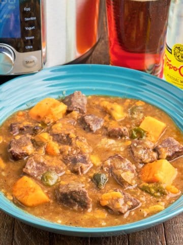 A bowl of beef stew with sweet potatoes and jalapeños, with an Instant Pot, a glass of beer, and a bottle of Top Chico in the background