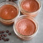 Three bittersweet chocolate pots de creme, with some chocolate chips on a gray tbable