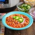 A bowl of ground buffalo chili, with an Instant Pot and sliced toppings in the background