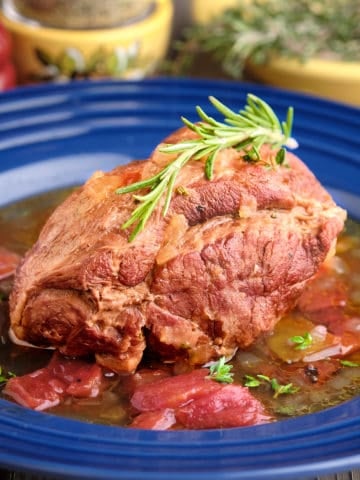 A piece of boneless leg of lamb, in sauce, with a sprig of rosemary on top