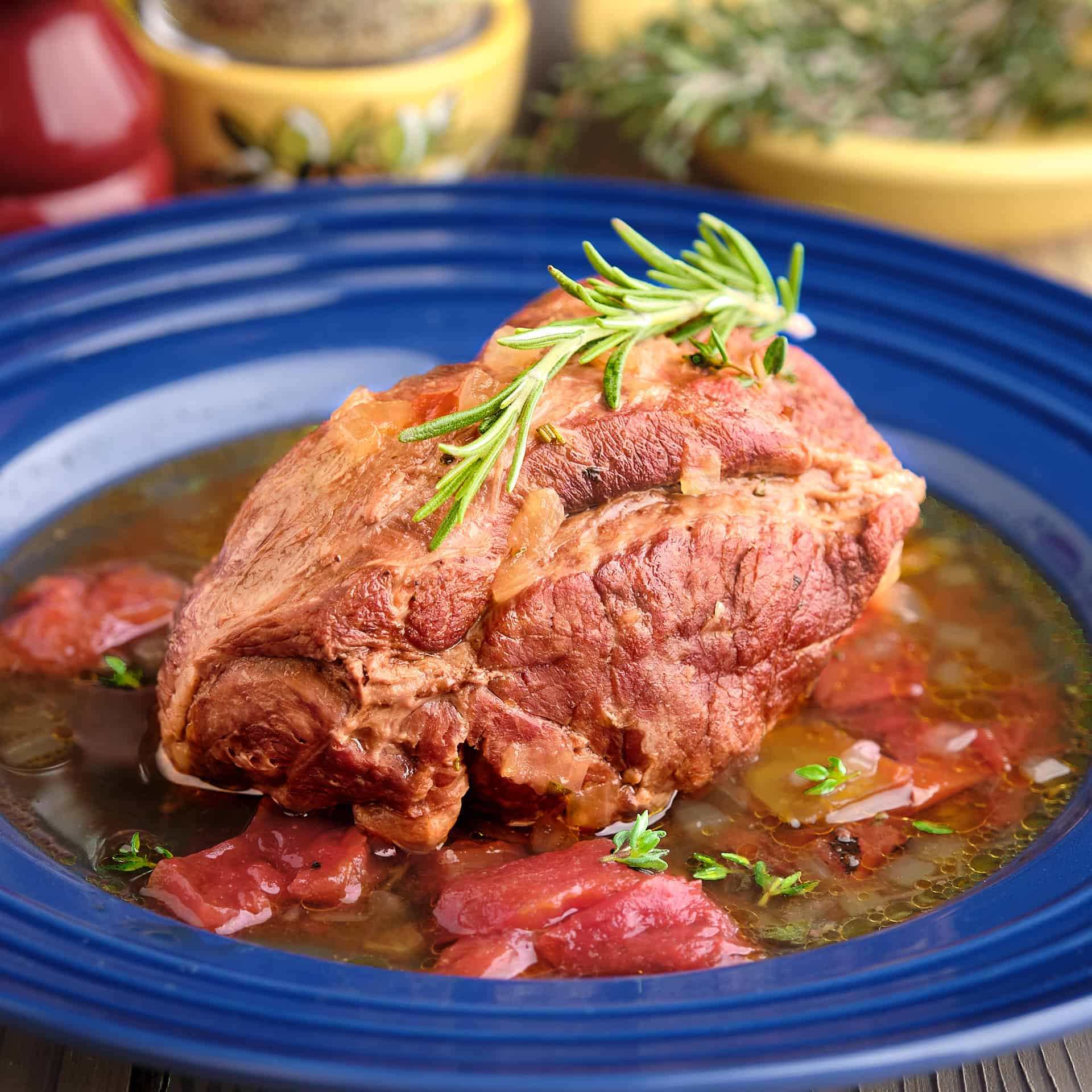 A piece of boneless leg of lamb, in sauce, with a sprig of rosemary on top