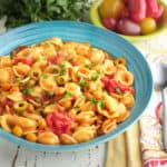 A bowl of chickpea puttanesca with orecchiette, with tomatoes, parsley, napkins, and a spoon