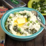 A bowl of colcannon with a big pat of butter, and more butter and greens in the background