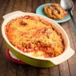 A baking dish of cranberry bean gratin, with a serving scooped out, and a plate with a scoop and some of the gratin in the background