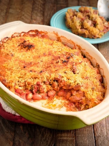 A baking dish of cranberry bean gratin, with a serving scooped out, and a plate with a scoop and some of the gratin in the background