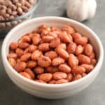 A bowl of cranberry beans, with a head of garlic and another bowl of dried cranberry beans in the background