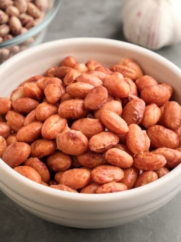 A bowl of cranberry beans, with a head of garlic and another bowl of dried cranberry beans in the background