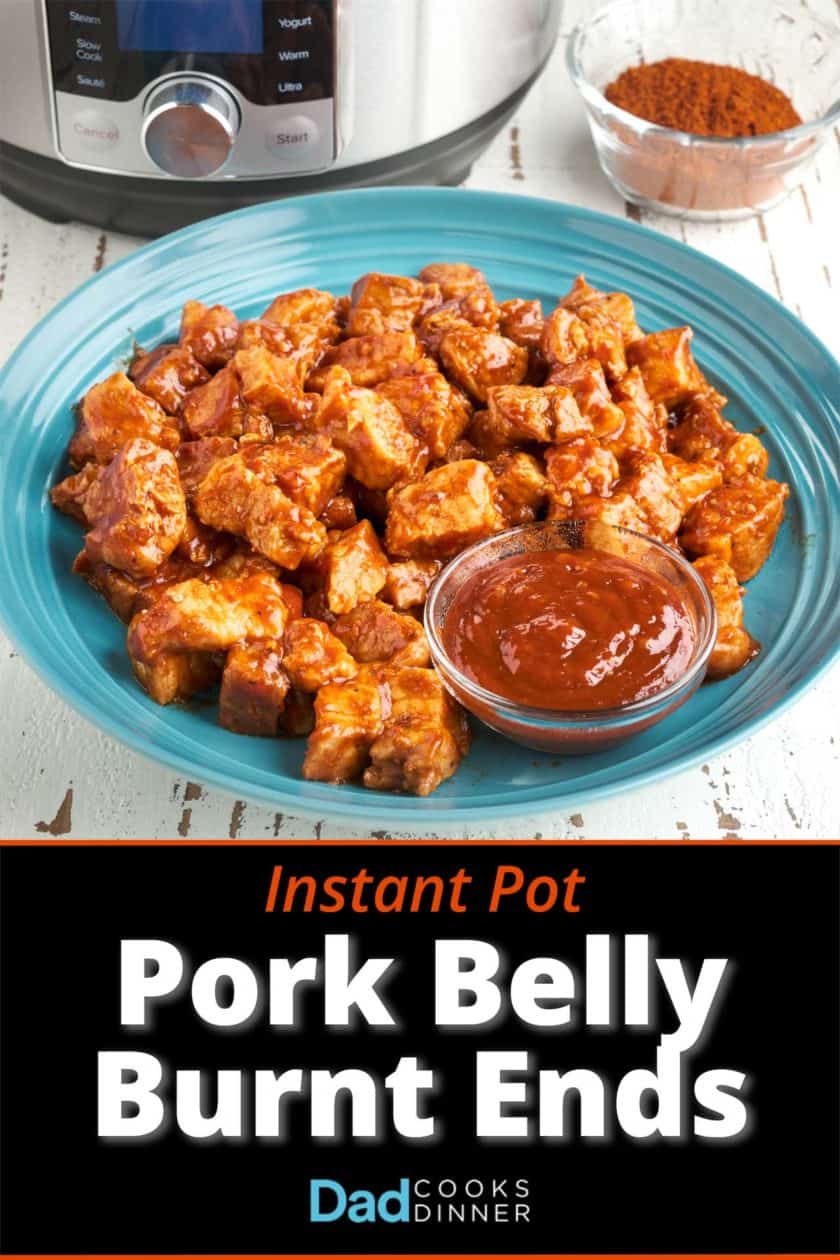 A bowl of pork belly cubes, tossed in barbecue sauce, with a small bowl of barbecue sauce, a bowl of barbecue rub, and a pressure cooker in the background