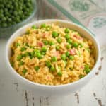 A bowl of rice and peas with more peas and a bag of vialone nano rice in the background