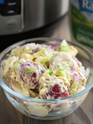 A bowl of ranch potato salad with an Instant Pot and bottle of dressing in the background