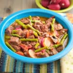 A bowl of beef stew with asparagus, carrots, and radishes.