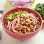 A bowl of white chili with sliced onions and jalapeños on top